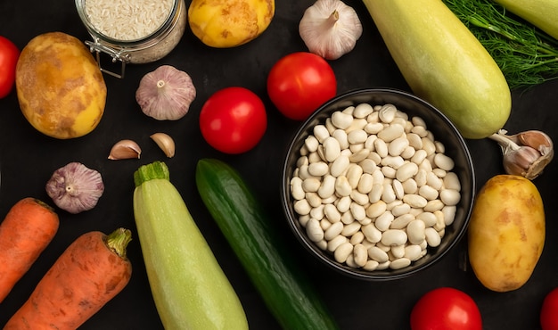 Haricot blanc cru avec des légumes frais sur fond noir. Nourriture saine végétarienne