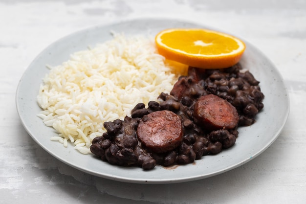 Haricots alimentaires brésiliens typiques avec saucisses et riz Feijoada sur plat blanc