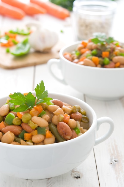 Haricots blancs aux légumes sur une table en bois blanche