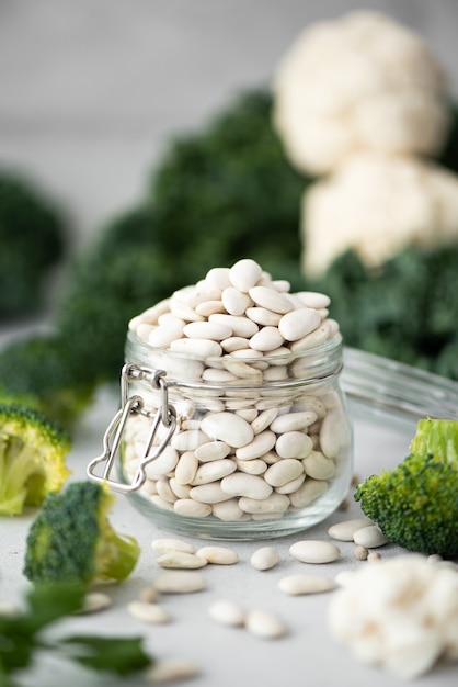 Haricots blancs dans un bocal en verre avec des légumes verts sur un tableau blanc