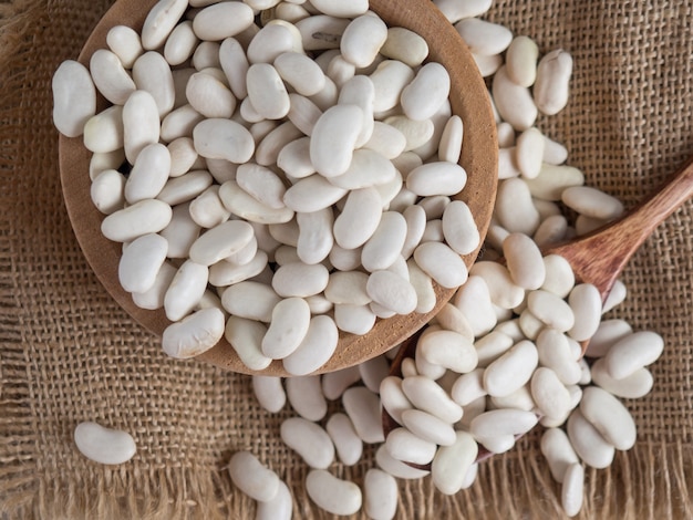 Haricots blancs dans une cuillère en bois sur une table en bois blanche, espace de copie