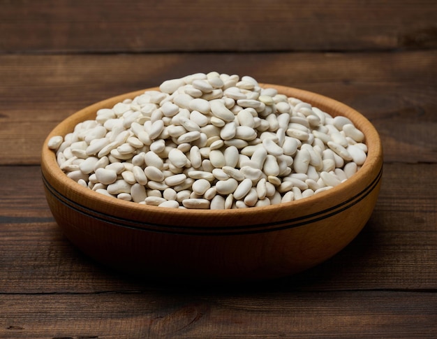 Haricots crus blancs dans une assiette en bois sur un fond en bois