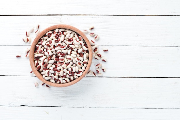 Haricots crus dans un bol sur un fond en bois blanc.