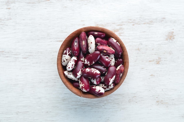 Haricots crus dans un bol sur un fond en bois blanc.