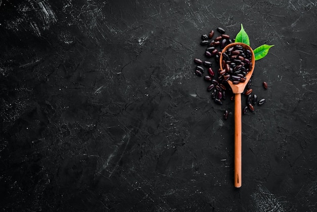 Haricots crus dans une cuillère en bois sur fond noir Vue de dessus Espace de copie gratuit