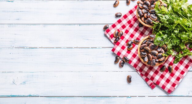 Haricots non cuits dans des bols en bois avec des herbes de persil sur la table de la cuisine.