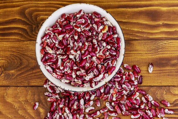 Haricots rouges crus dans un vieux bol émaillé blanc sur une table en bois