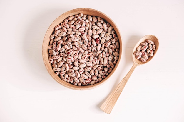 Haricots secs crus dans un bol en bois avec une cuillère sur un fond blanc