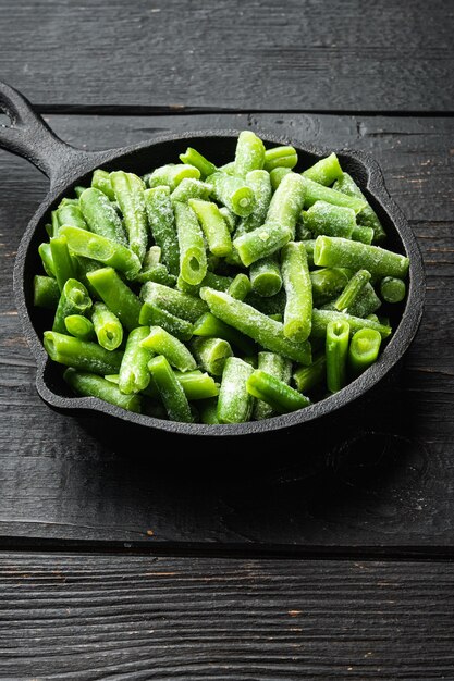 Haricots verts. Haricots frais congelés pour salade, cuisine ou ensemble d'aliments végétaliens crus, dans une poêle en fonte, sur une table en bois noir