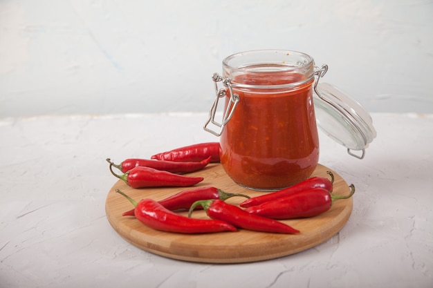 Harissa dans un bocal en verre sur un support en bois et piments forts.