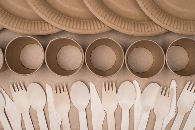 En haut au-dessus de la photo vue de dessus de rangées de couverts en bois, de gobelets en papier et d'assiettes isolées sur une table d'arrière-plan en papier kraft