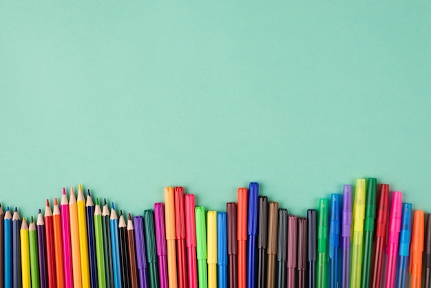 En haut au-dessus de la vue aérienne flatlay photo de crayons et marqueurs multicolores isolés sur fond turquoise avec copyspace