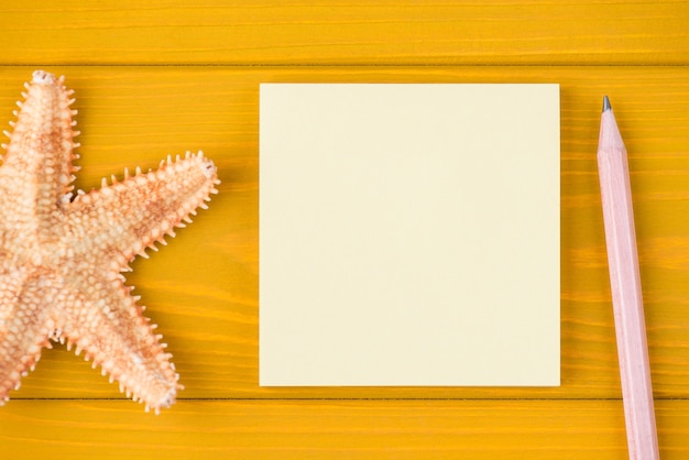 Haut au-dessus de la vue aérienne photo recadrée en gros plan d'une note vierge d'étoile de mer et d'un crayon isolé sur fond de bois jaune avec fond