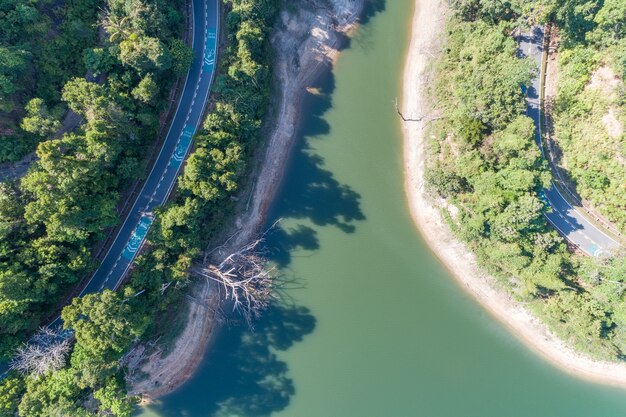 Photo de haut en bas depuis le drone vue aérienne de la forêt tropicale avec route goudronnée autour du barrage et des terres partagées, méfiez-vous du signe de vélo sur la route.