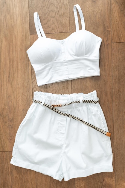 Haut blanc pour femme avec bretelles dans un style élégant et short blanc avec une ceinture tressée sur un fond en bois Vue de face Vue de dessus