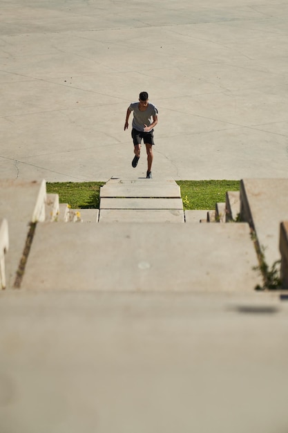 D'en haut, un coureur masculin éloigné en vêtements de sport court sur un escalier en pierre pendant un entraînement intense dans la rue de la ville