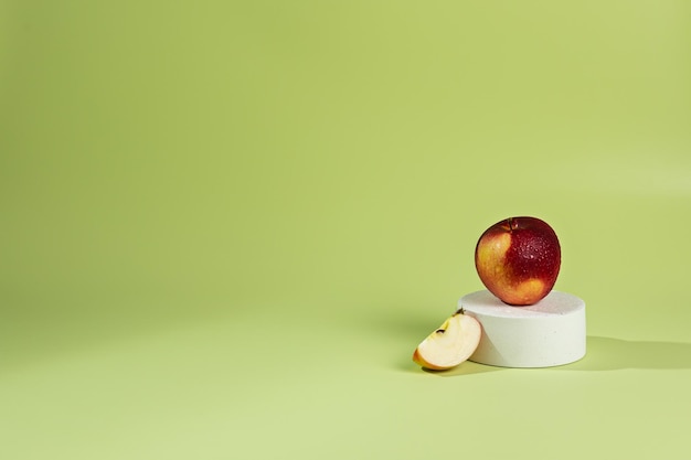 Sur un haut-de-forme de podium blanc, il y a une pomme rouge sur fond vert et une ombre du soleil