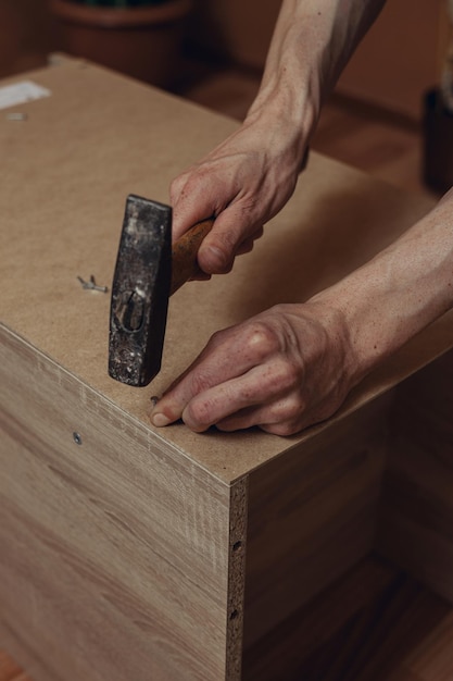 D'en haut, un homme de récolte martelant un clou dans une planche de bois lors de l'assemblage d'une nouvelle table à la maison