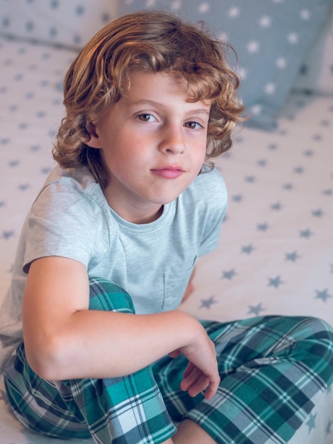 D'en haut, un petit garçon en pyjama assis sur le lit et regardant la caméra