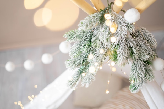 Le haut des tippies enfant est orné de pompons en branches de sapin et d'une guirlande fond de Noël en bokeh