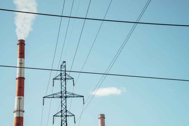 Le haut tube rayé rouge et blanc laisse sortir la fumée blanche dans un ciel bleu clair. Petit nuage au-dessus du tuyau sur fond de poteau électrique et de fils d'alimentation. Gros plan de centrale thermique avec espace de copie.