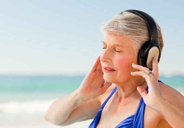 Haute femme écoutant de la musique à la plage