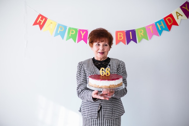 Haute femme fête son birthay à la maison. Tenant un gâteau d&#39;anniversaire sur fond blanc