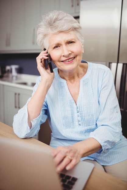 Haute femme parlant au téléphone et utilisant un ordinateur portable dans la cuisine