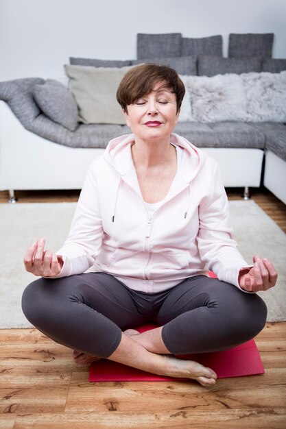 Haute femme pratiquant le yoga à la maison