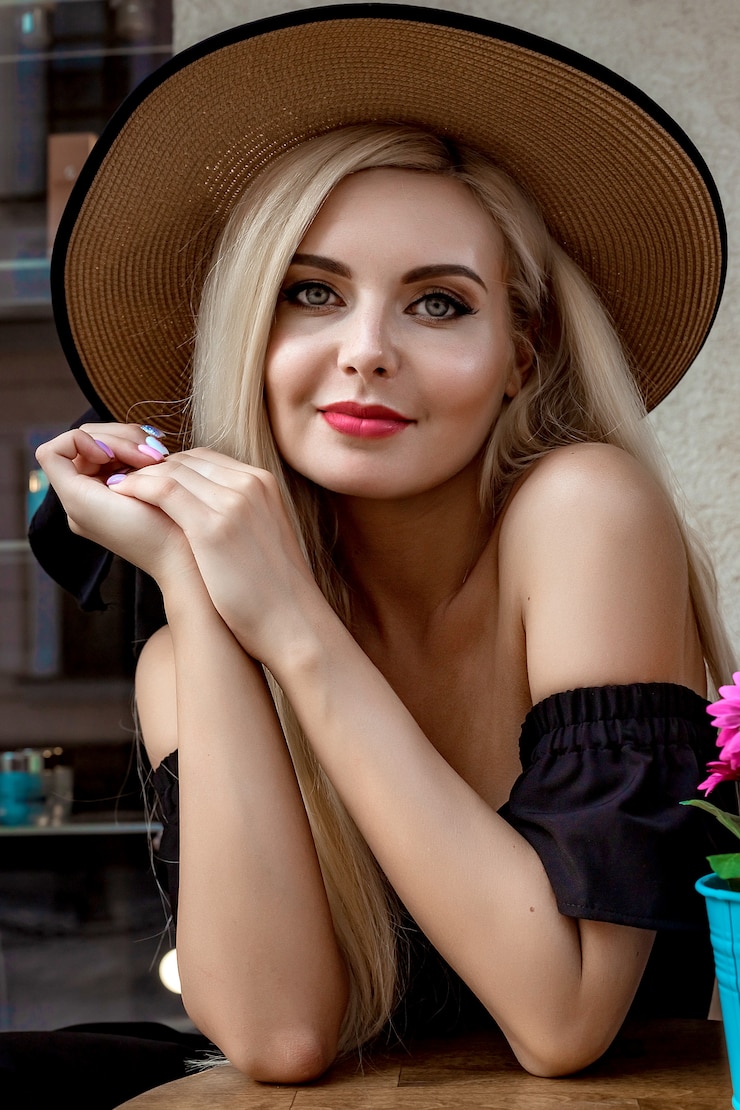 Photo haute mode portrait d'une femme gracieuse dans un élégant chapeau de paille et une robe qui se trouve dans un café à une table