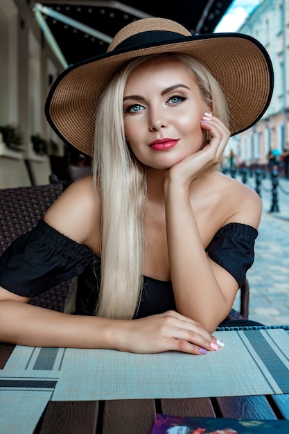 Haute mode portrait d'une femme gracieuse dans un élégant chapeau de paille et une robe qui se trouve dans un café à une table