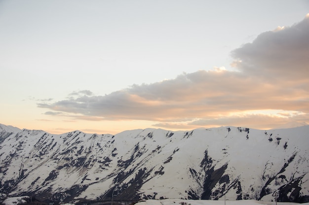 De hautes montagnes avec des pics enneigés contre un beau ciel d'avant l'aube avec des nuages