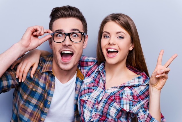 Hé, assez de triste! Beau jeune couple d'amoureux gesticulant et souriant à la caméra en se tenant debout sur fond gris