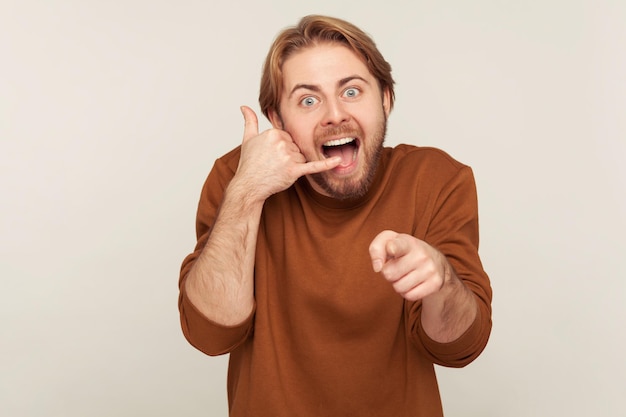 Hé, tu m'appelles Portrait d'un homme heureux étonné tenant le geste de la main du téléphone près de l'oreille et pointant vers l'appareil photo