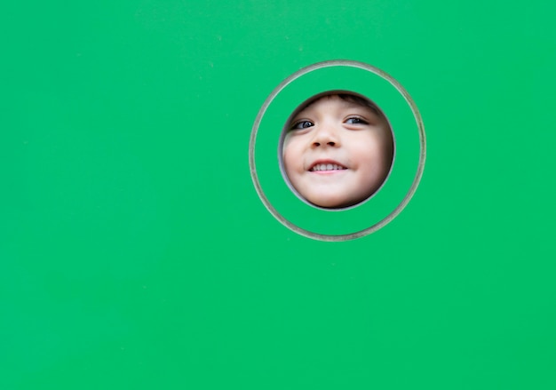 Head shot Happy kid montrant son visage dans un hublot sur fond vert.