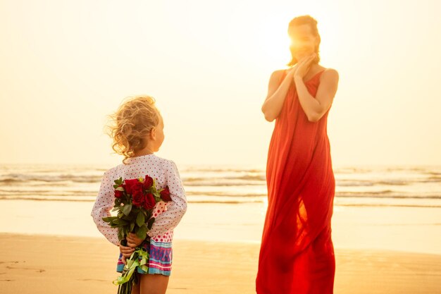 Héhé avec bouquet de fleurs roses sur la plage au bord de la mer au coucher du soleil. Jeune belle mère et fille étonnées félicitant joyeux anniversaire. Saint Valentin, 8 mars Journée internationale de la femme