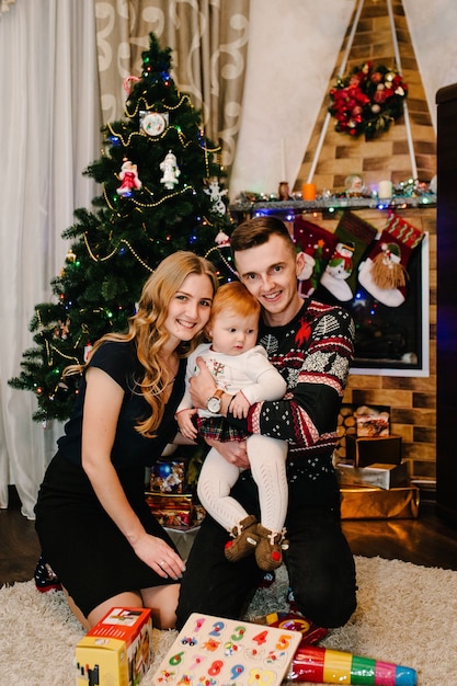 Héhé: maman, papa et fille près de l'arbre de Noël avec des cadeaux et une cheminée. Concept de nouvel an. Joyeux Noël.