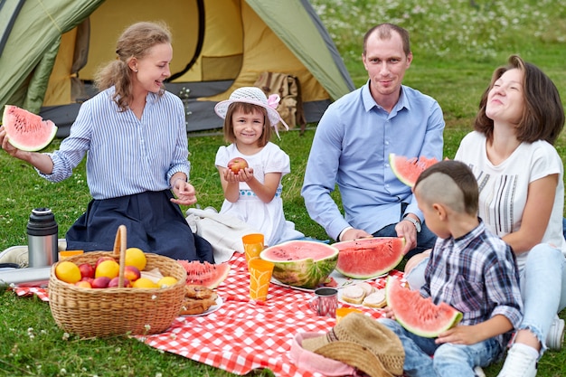 Héhé, manger la pastèque au pique-nique dans le pré près de la tente. Famille profitant de vacances en camping à la campagne