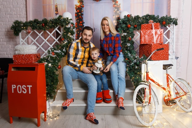 Héhé posant sur un porche décoratif. Fête de Noël à la maison. Maman, papa et fils portaient en tenue décontractée. Famille heureuse drôle jouant dans leur maison. Intérieur de maison décoré de Noël