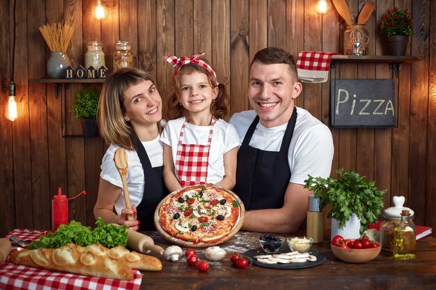 Héhé en tabliers souriant et tenant une pizza cuite