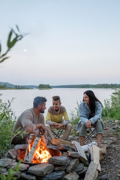 Héhé de trois personnes assises près d'un feu de camp contre le lac