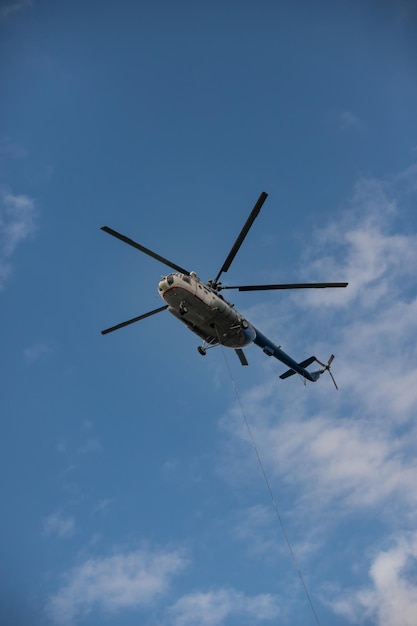 Un hélicoptère blanc et bleu volant dans le ciel bleu le câble sort de l'hélicoptère