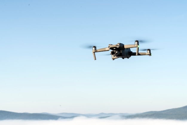 hélicoptère quadcopter drone dans les airs, dans un ciel bleu clair, brouillard matinal et montagnes en contrebas. prise de vue aérienne et vidéo à l'aide de gadgets et d'appareils modernes.