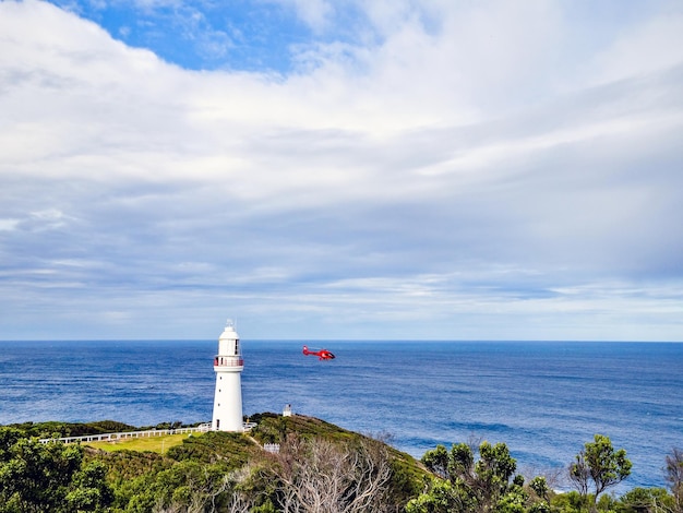 Photo hélicoptère volant près du phare par la mer contre le ciel