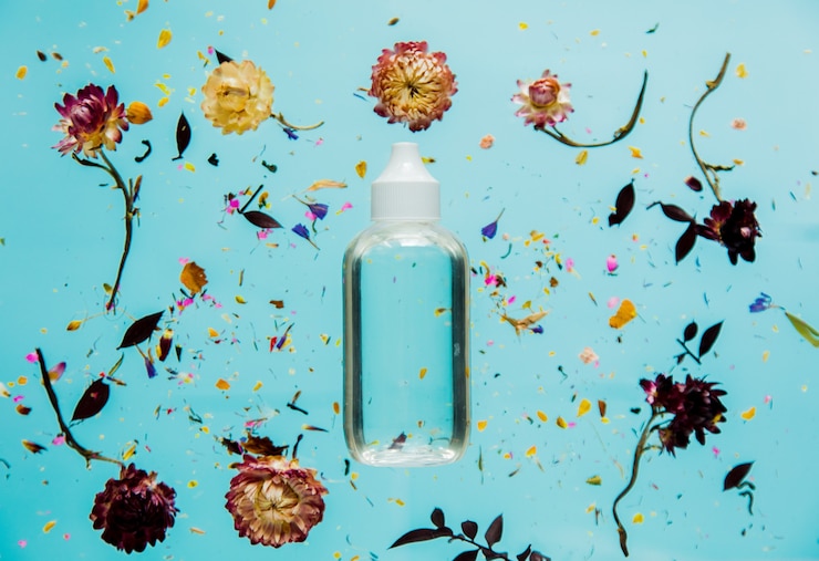 Photo herbe sèche de bellis avec des fleurs et une bouteille transparente sur une surface bleue isolée. sans ombres