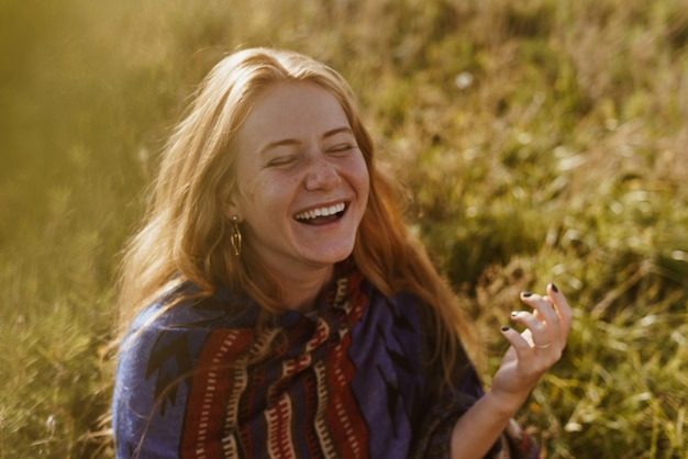 Sur l'herbe de la steppe se trouve une fille de beauté naturelle naturelle avec de longs cheveux rouges dans une cape ethno et co