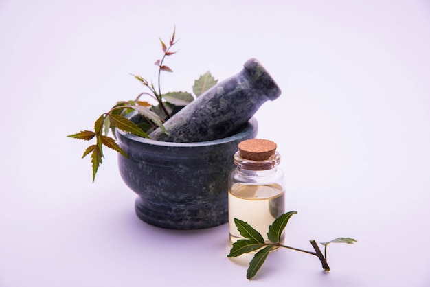 Photo herbes antibactériennes ayurvédiques neem ou lilas ou azadirachta indica avec de l'huile en bouteille avec du mortier, isolées sur fond uni, mise au point sélective
