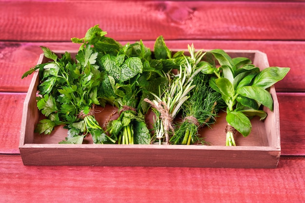 Herbes dans un plateau en bois sur une table rustique rouge