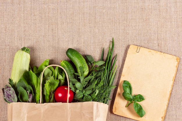 Herbes et légumes biologiques dans un sac en papier et une feuille de papier vintage avec des feuilles de basilic dessus