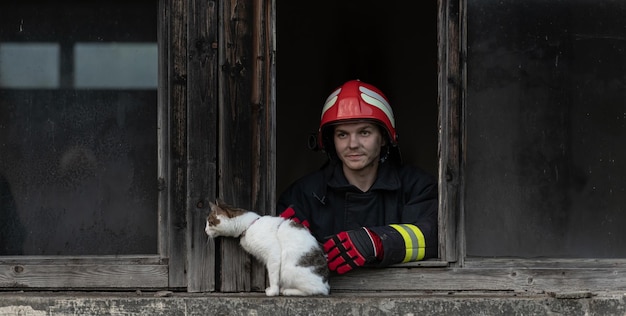 Héros pompier transportant un chat hors de la zone de construction en feu après l'incendie. Sauver un animal d'un endroit dangereux. Notion de travail d'équipe. Photo de haute qualité